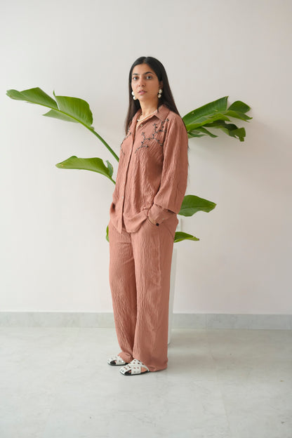 Woman in a pink outfit standing next to a plant against a white wall