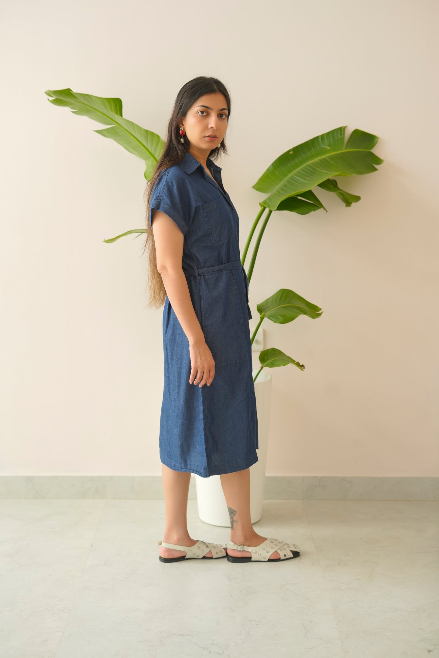 Woman wearing a blue dress standing next to a large green plant indoors.