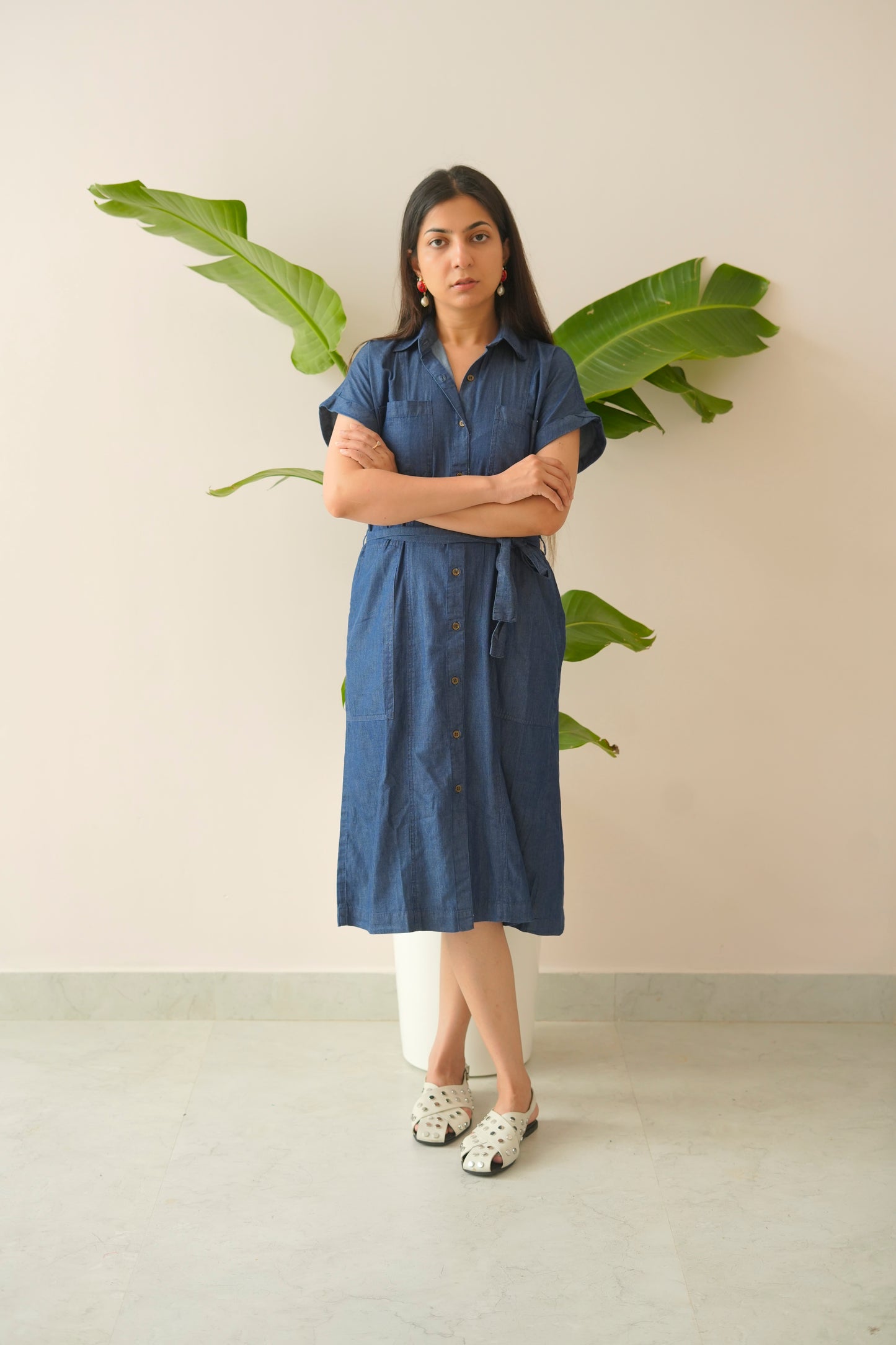 Woman in a blue dress standing in front of a plant with a neutral background