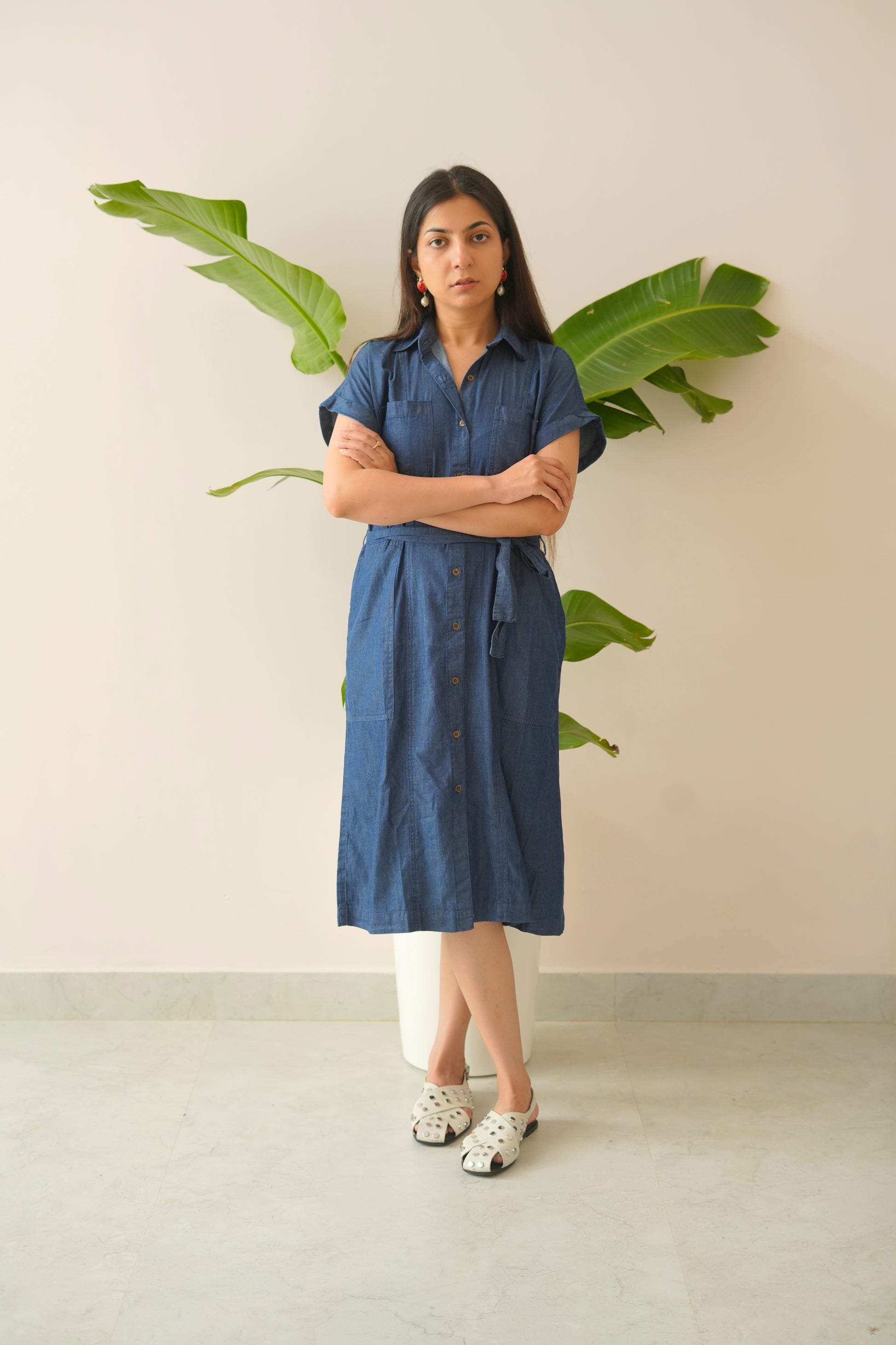 Woman in a blue dress standing in front of a plant with a neutral background