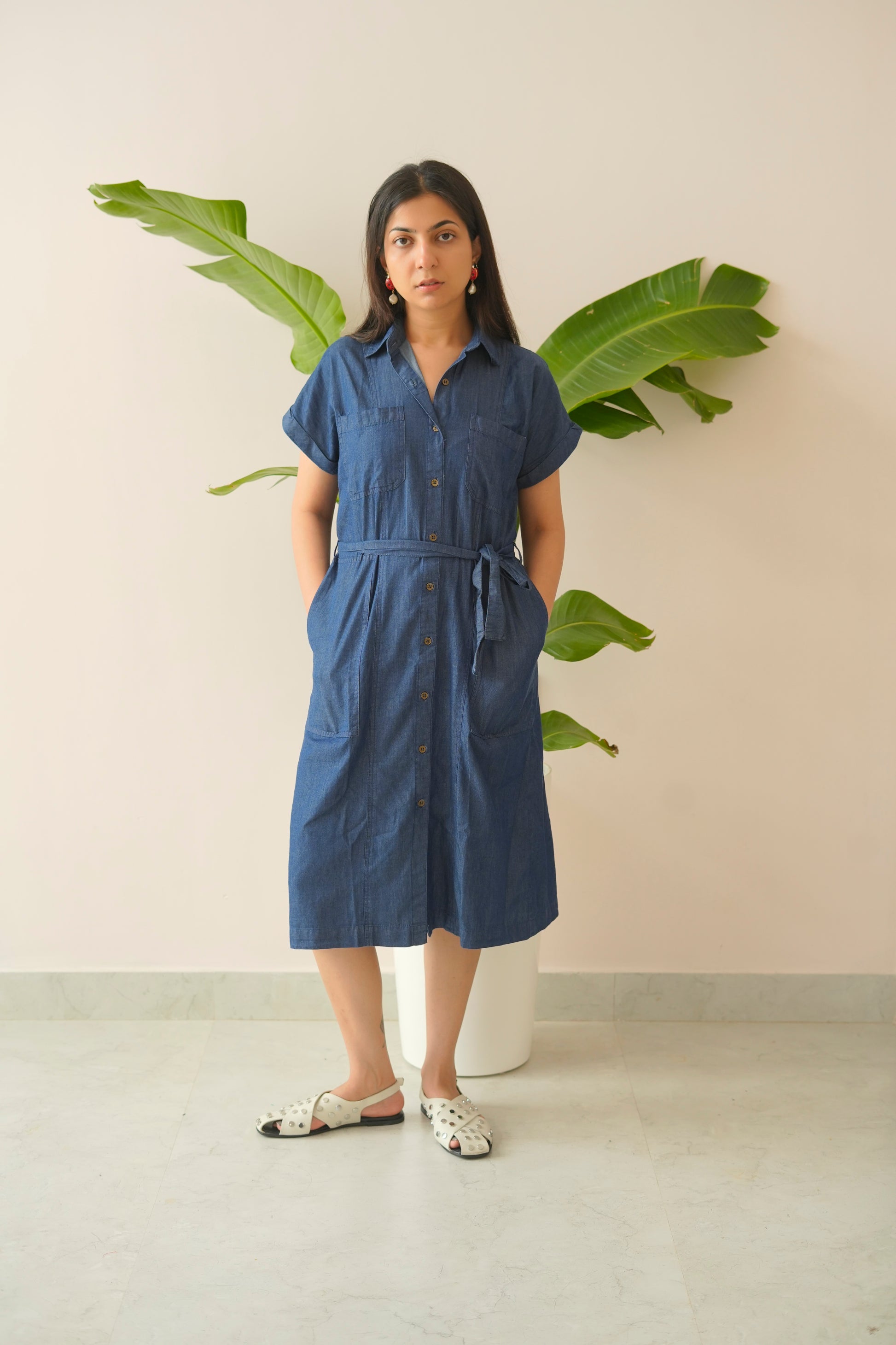 Woman wearing a blue dress standing in front of a plant against a light background