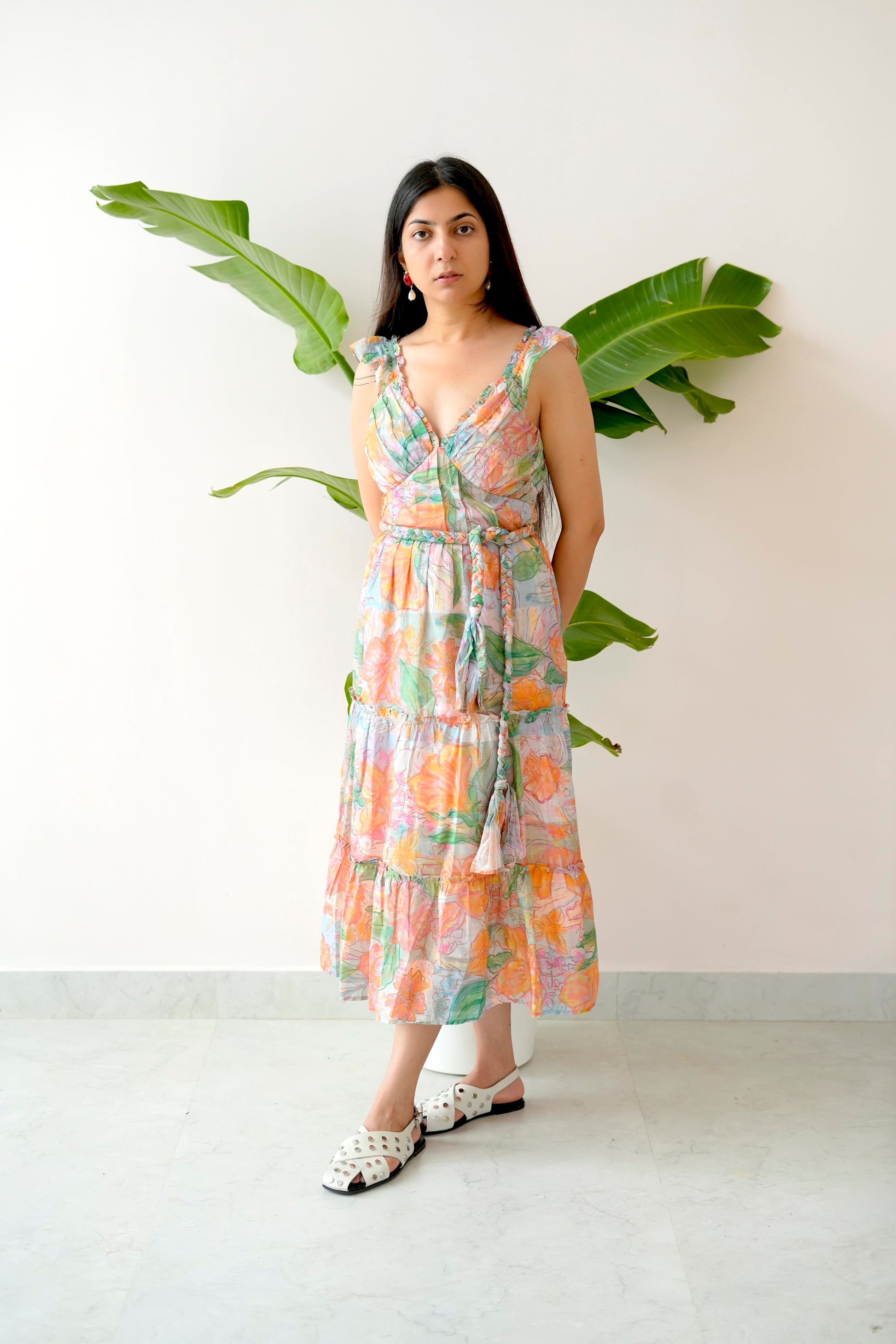 Woman wearing a floral dress standing against a white wall with green leaves.
