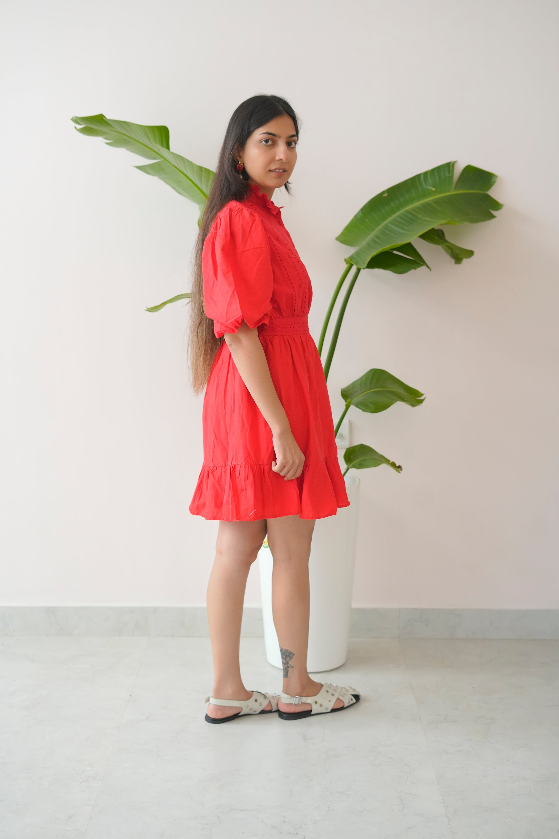 Woman in a red dress standing next to a plant against a white wall