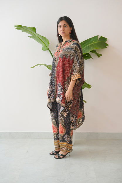 Woman wearing a patterned outfit standing against a white wall with a plant.