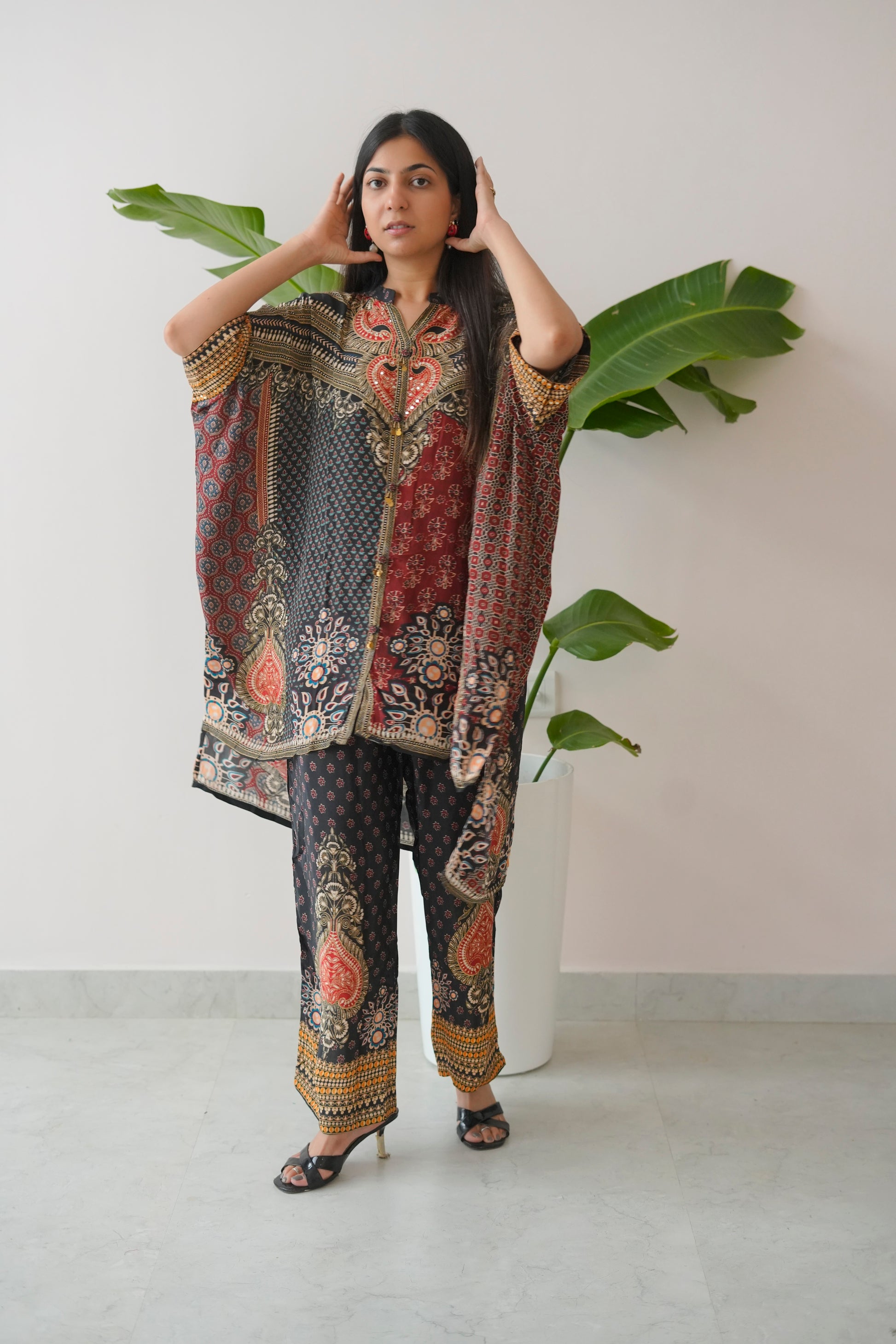 Woman wearing a patterned outfit with a white background and green plants.