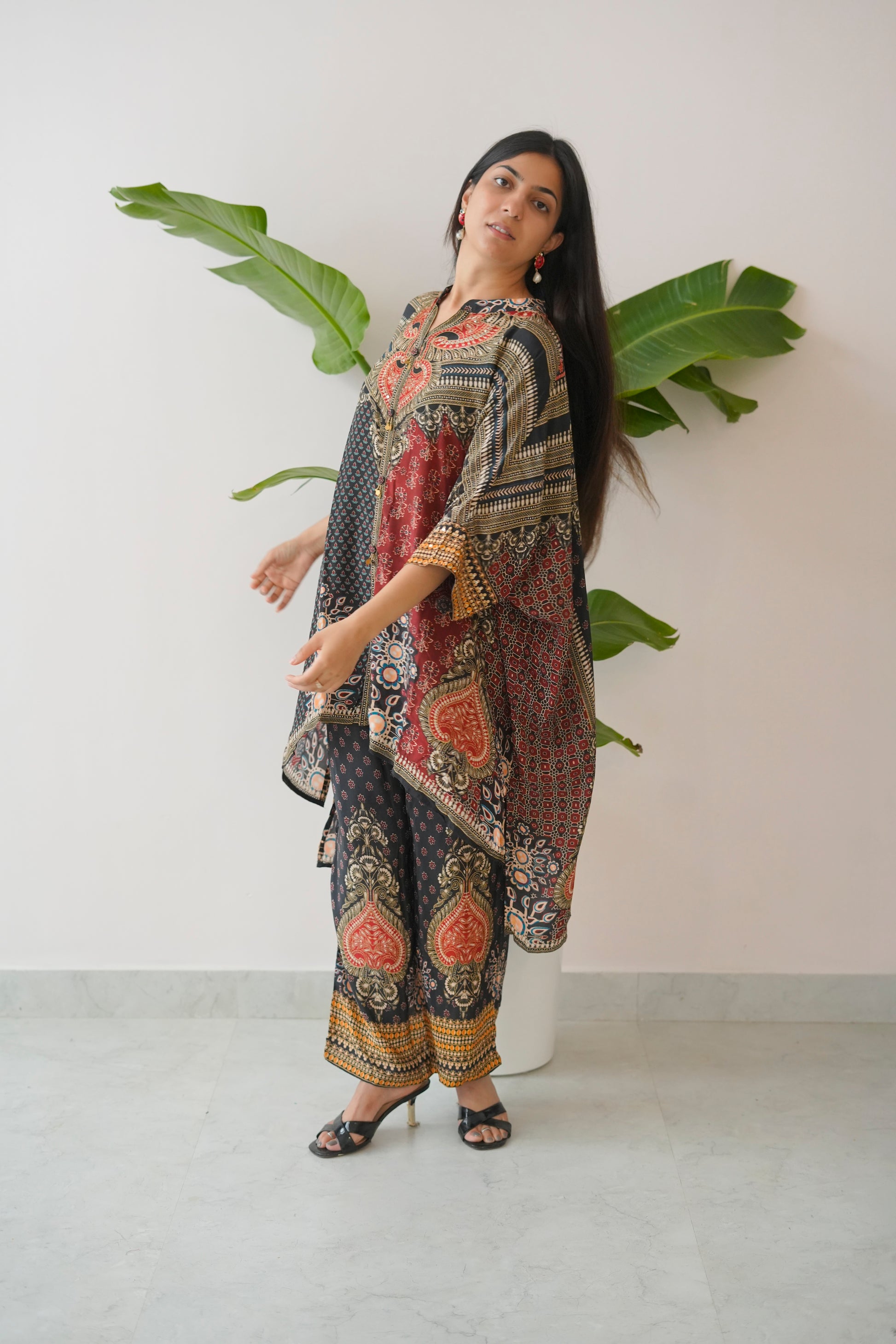 Woman wearing a patterned dress standing against a white wall with a plant.