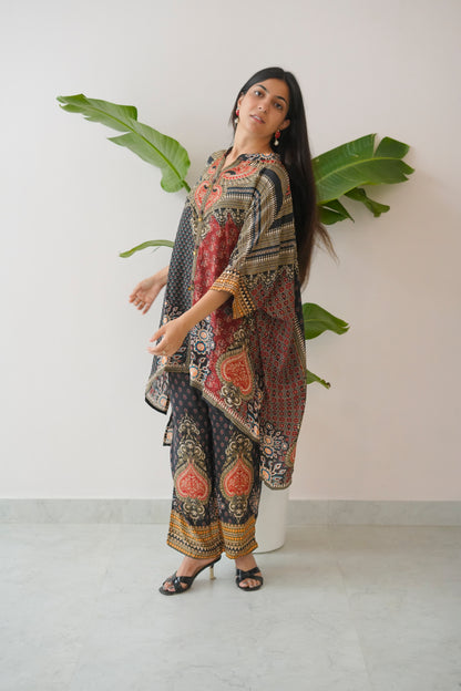 Woman wearing a patterned dress standing against a white wall with a plant.