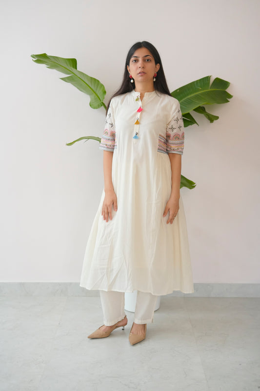 Woman wearing a white kurta with colorful details against a plain background