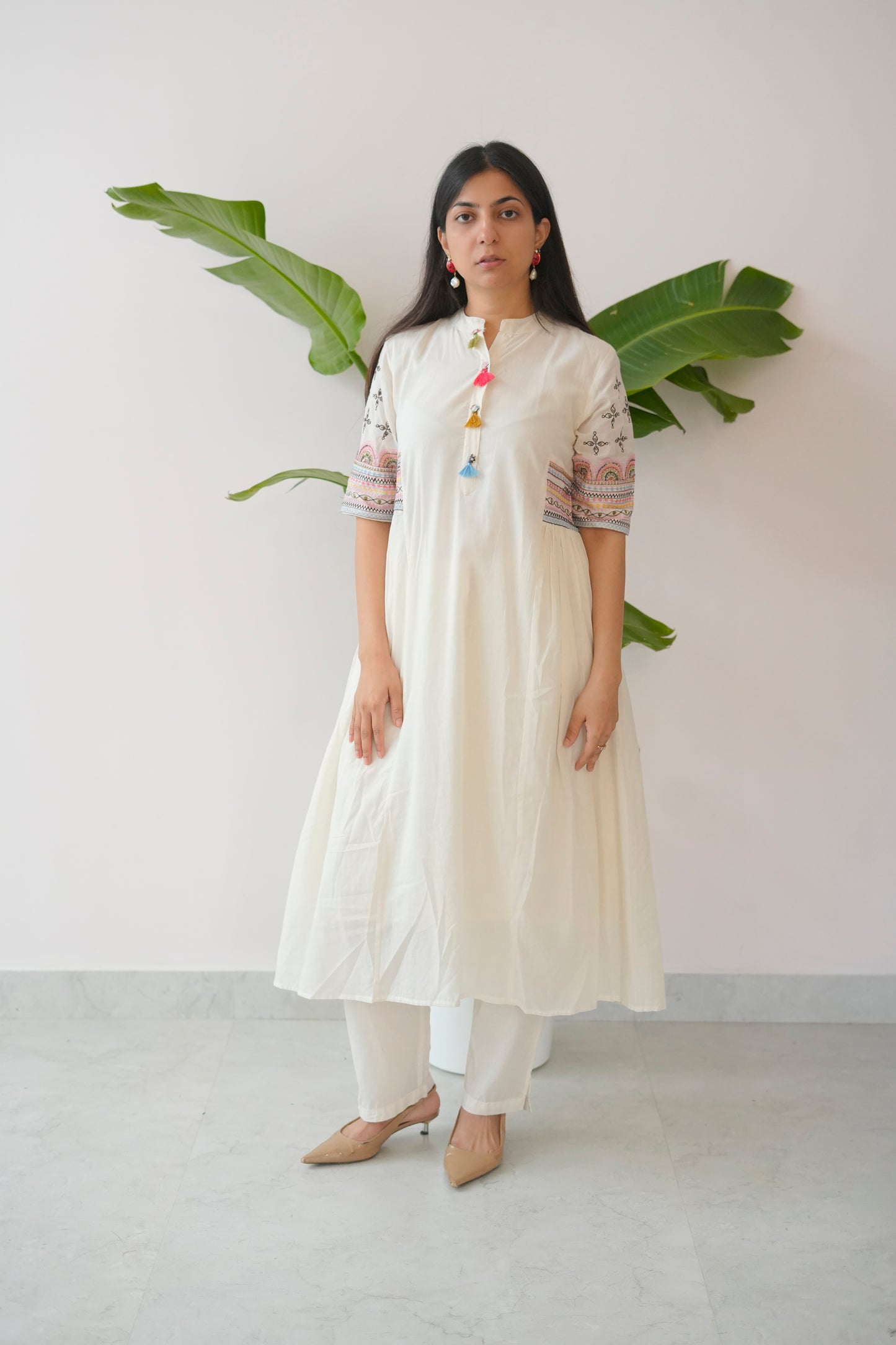 Woman wearing a white kurta with colorful details against a plain background