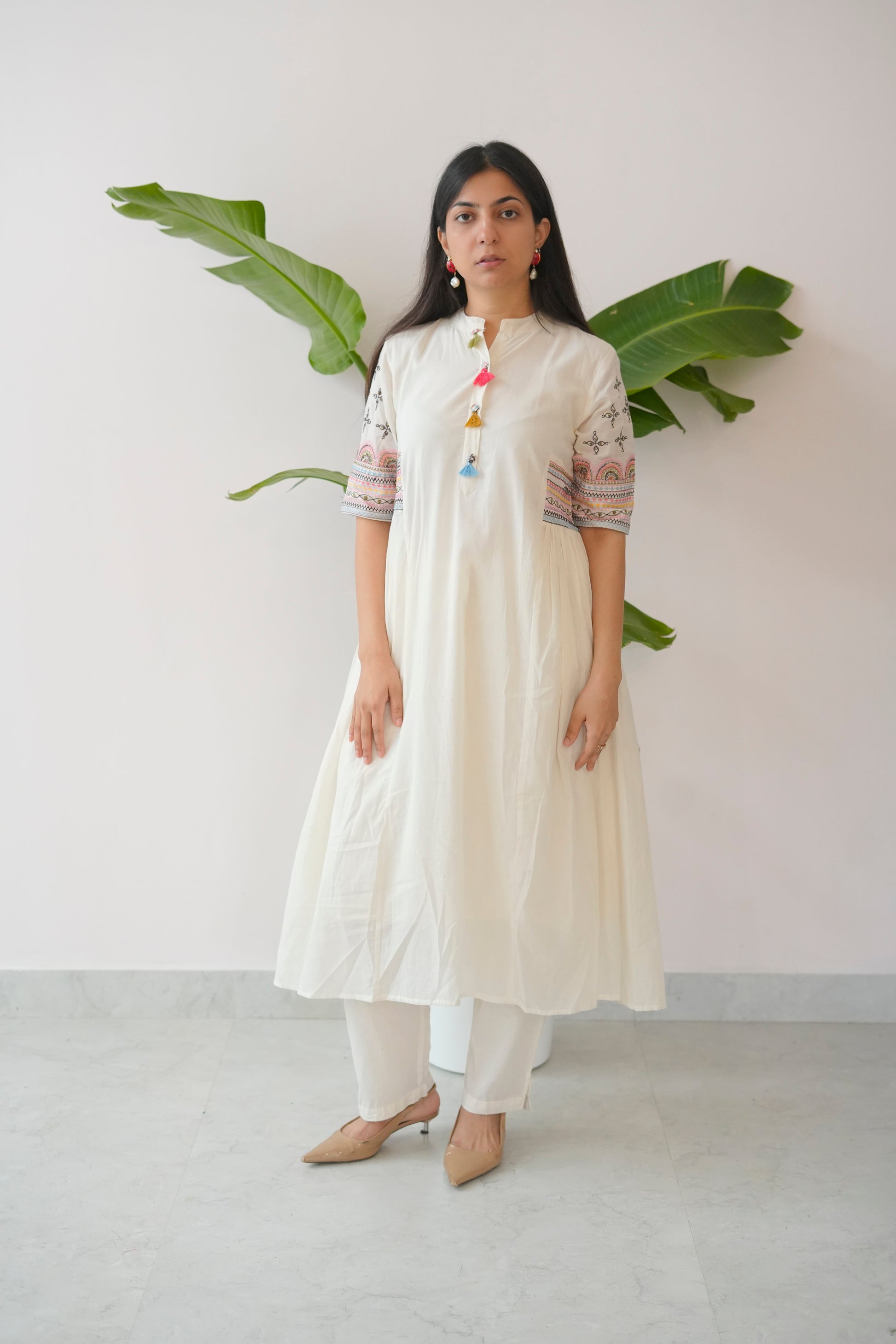 Woman wearing a white kurta with colorful details against a plain background