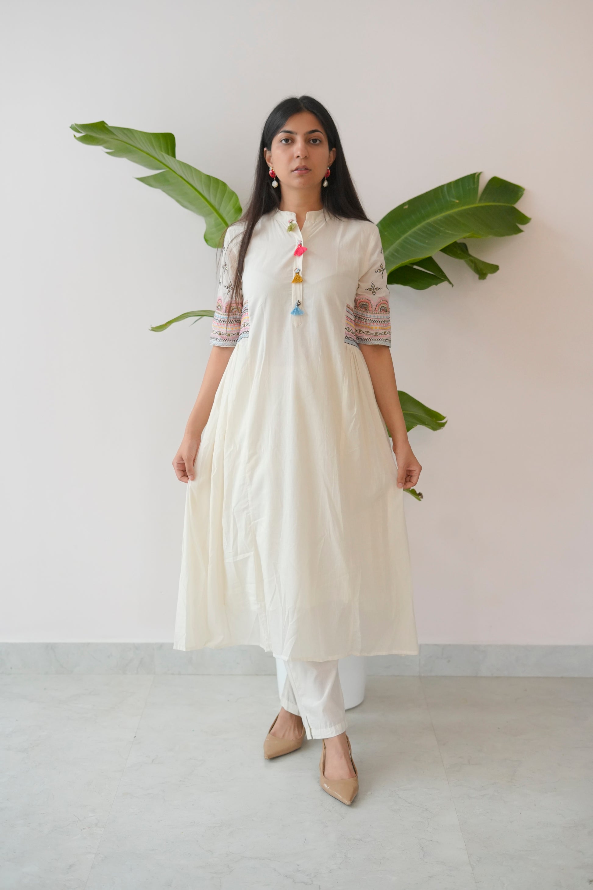 Woman wearing a white dress with colorful accents against a plain background