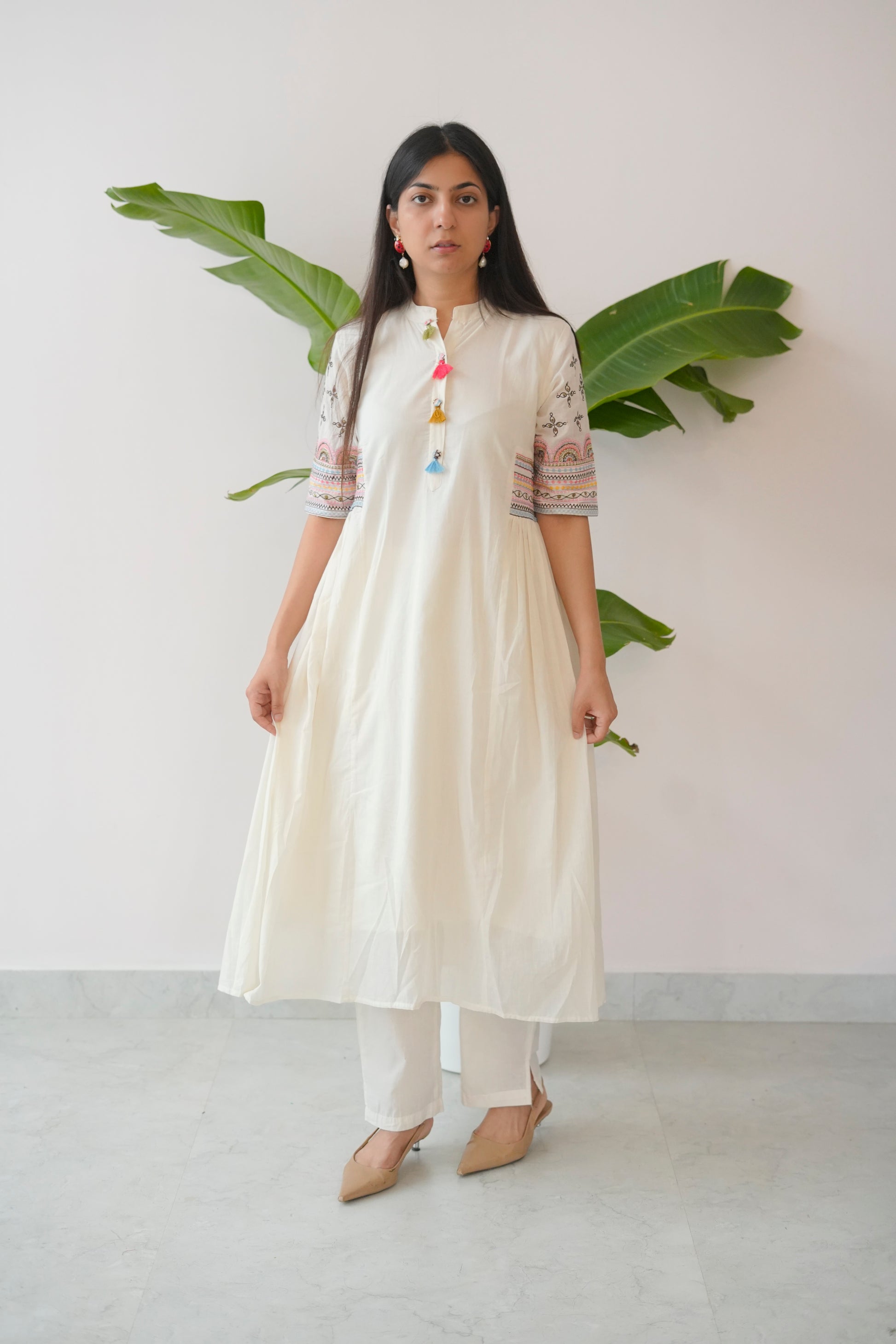 Woman wearing a white outfit with colorful details against a plain background