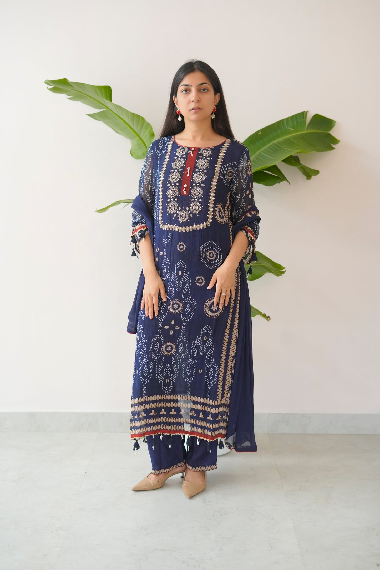 Woman wearing a blue embroidered traditional outfit with a white background and green leaves.
