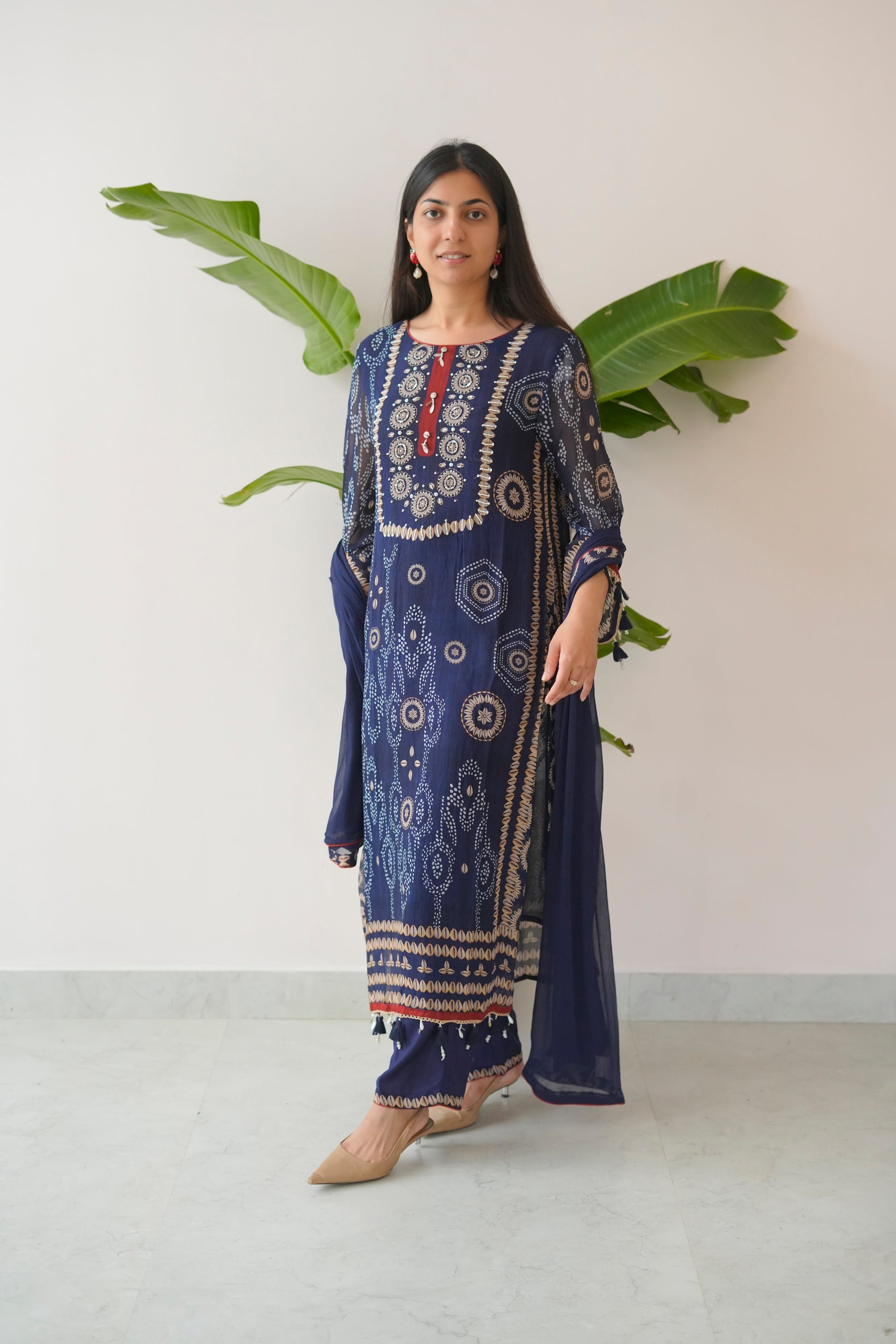 Woman wearing a blue embroidered traditional outfit with a white background and green leaves.