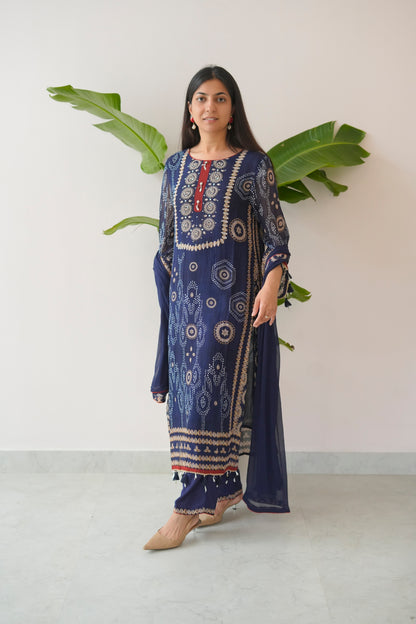 Woman wearing a blue embroidered traditional outfit with a white background and green leaves.