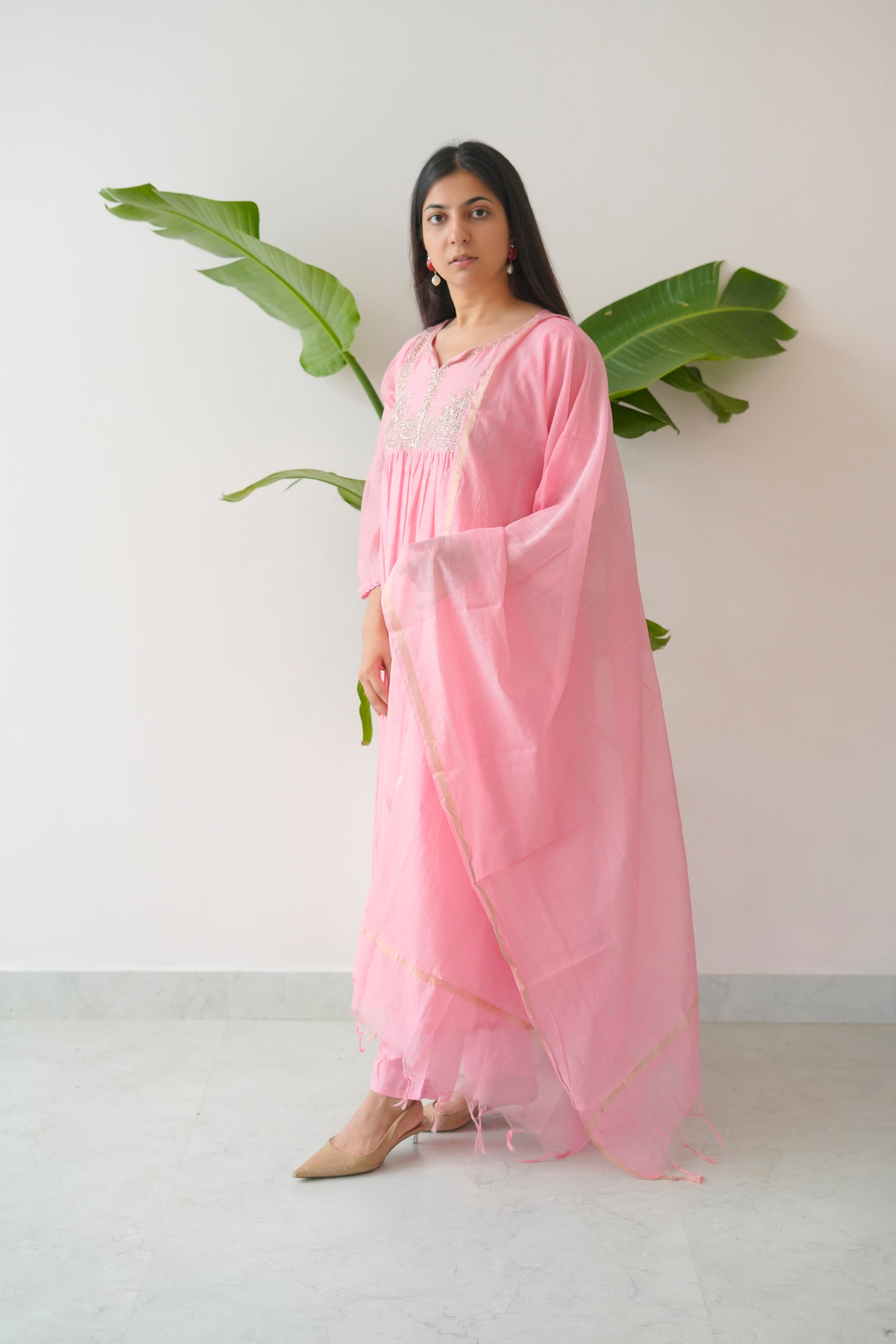 Woman wearing a pink saree with a white background and green leaves.