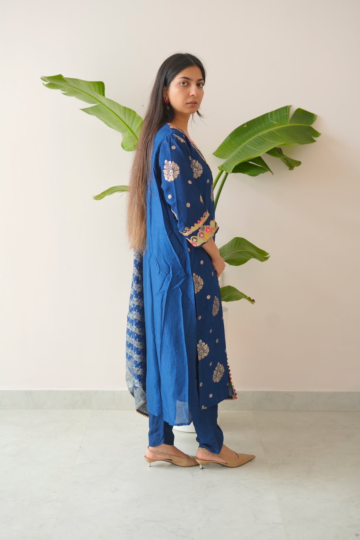 Woman in a blue traditional outfit holding a plant against a white wall