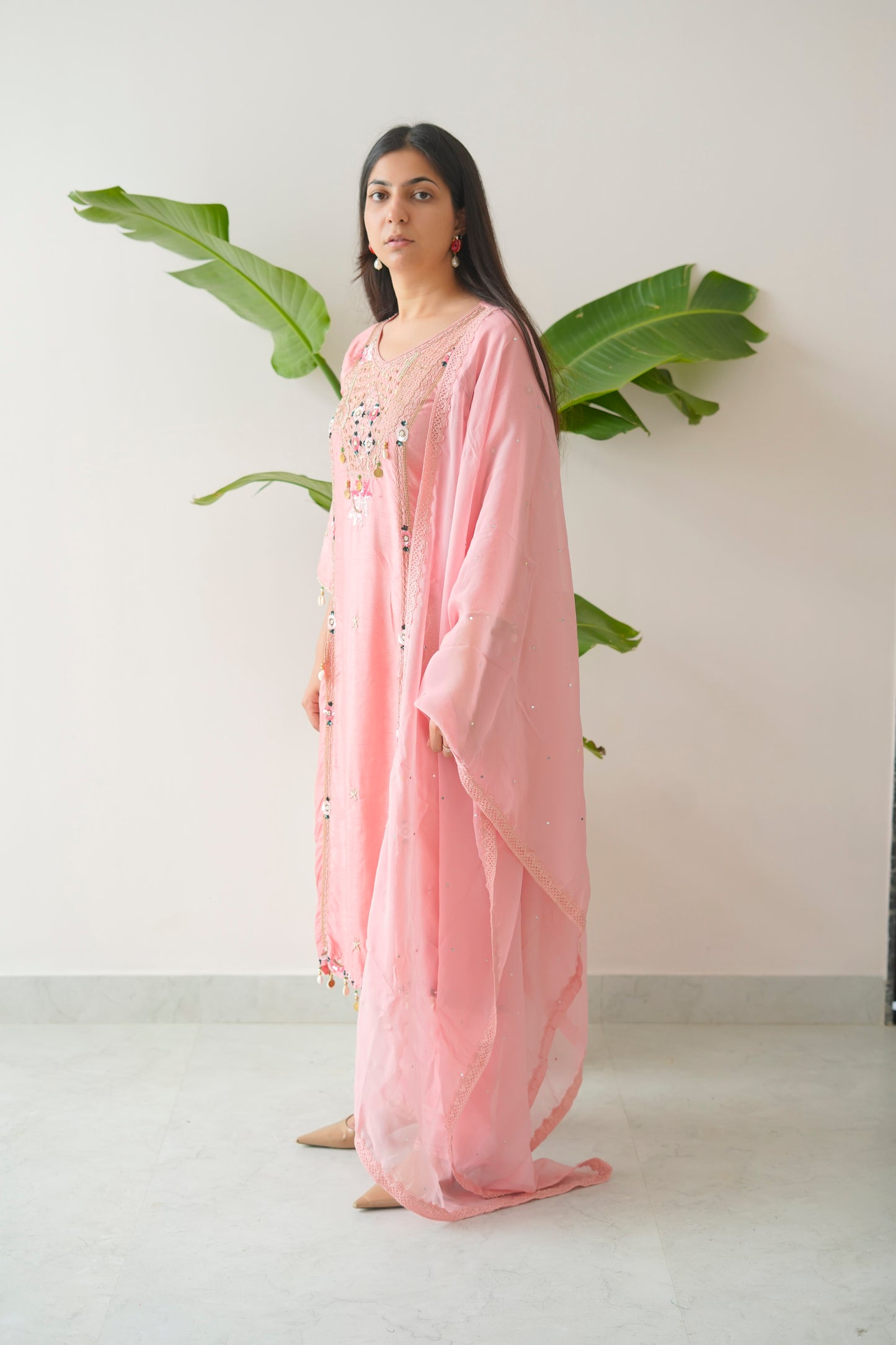 Woman wearing a pink dress with a white background and green leaves.