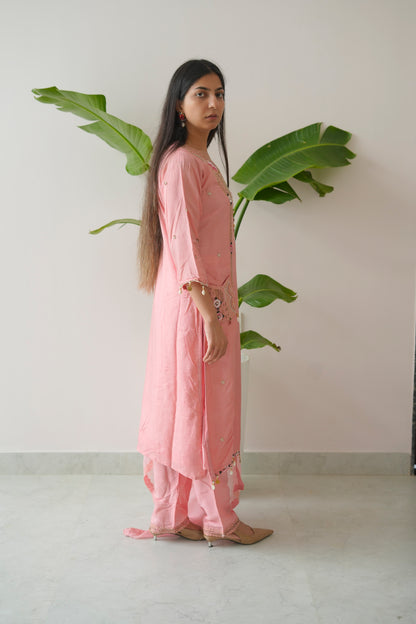 Woman in a pink outfit standing next to a large green leafy plant indoors.