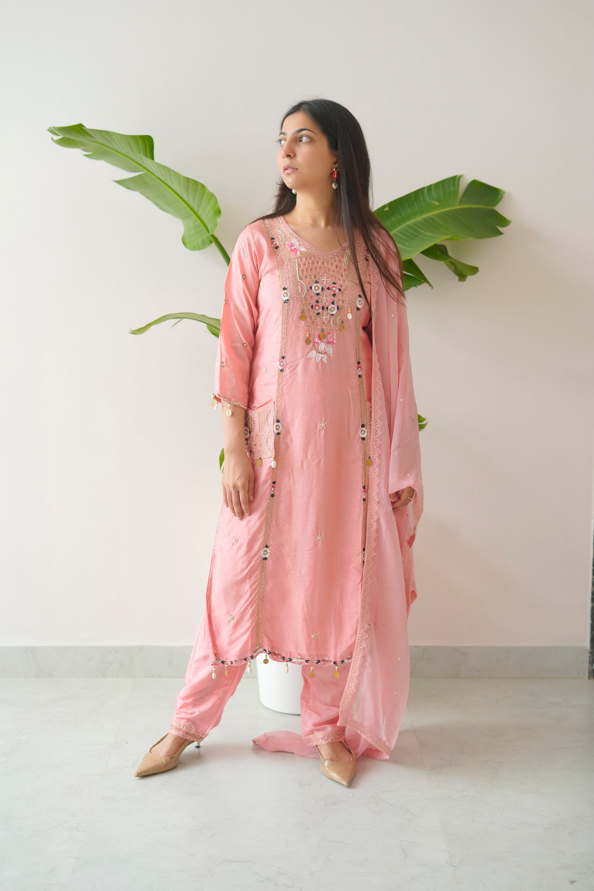 Woman wearing a pink embroidered traditional outfit with a white background and green leaves.