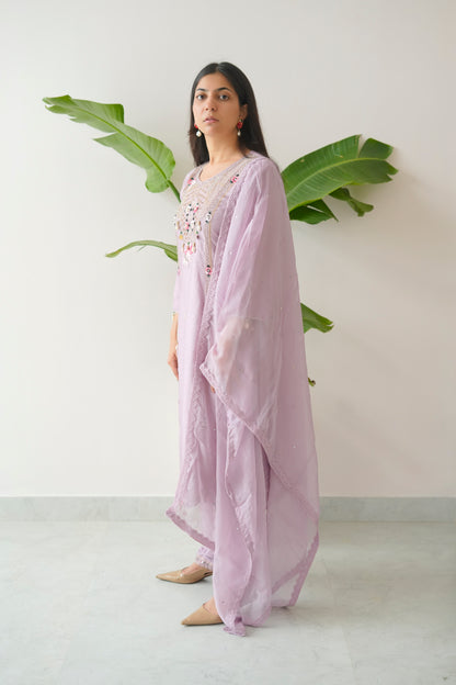 Woman wearing a light purple traditional outfit with a white background and green leaves.