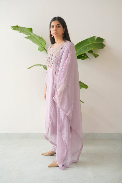 Woman wearing a light purple outfit with floral embellishments against a white background