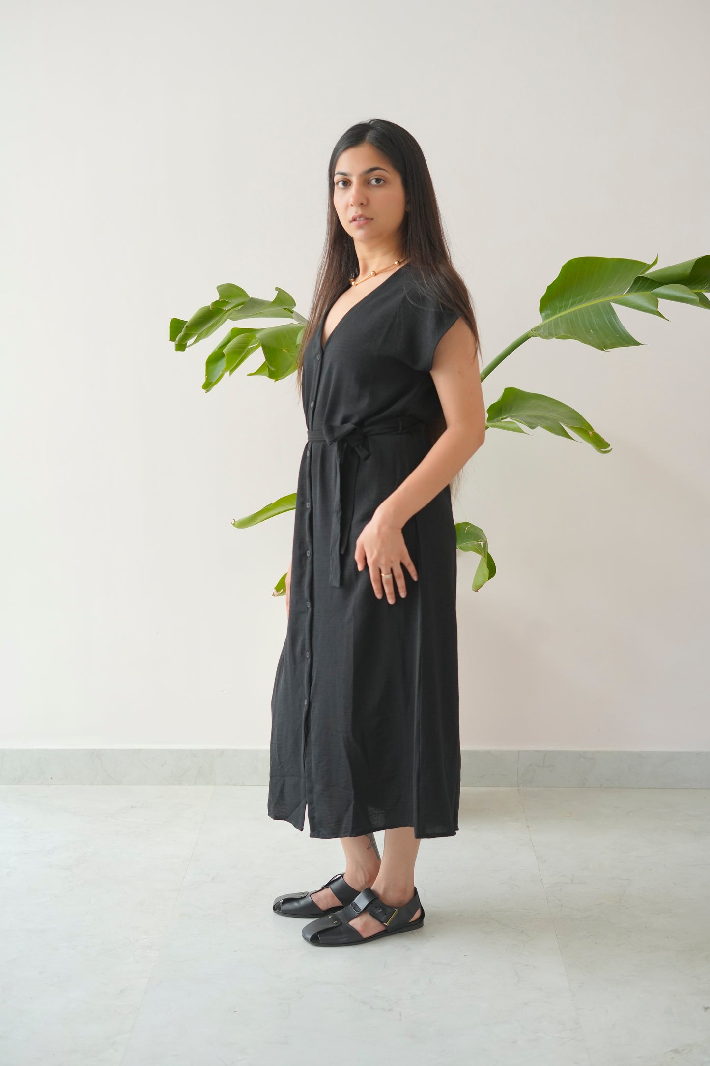 Woman wearing a black dress standing in front of a plant with a white wall background