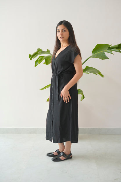 Woman wearing a black dress standing in front of a plant with a white wall background