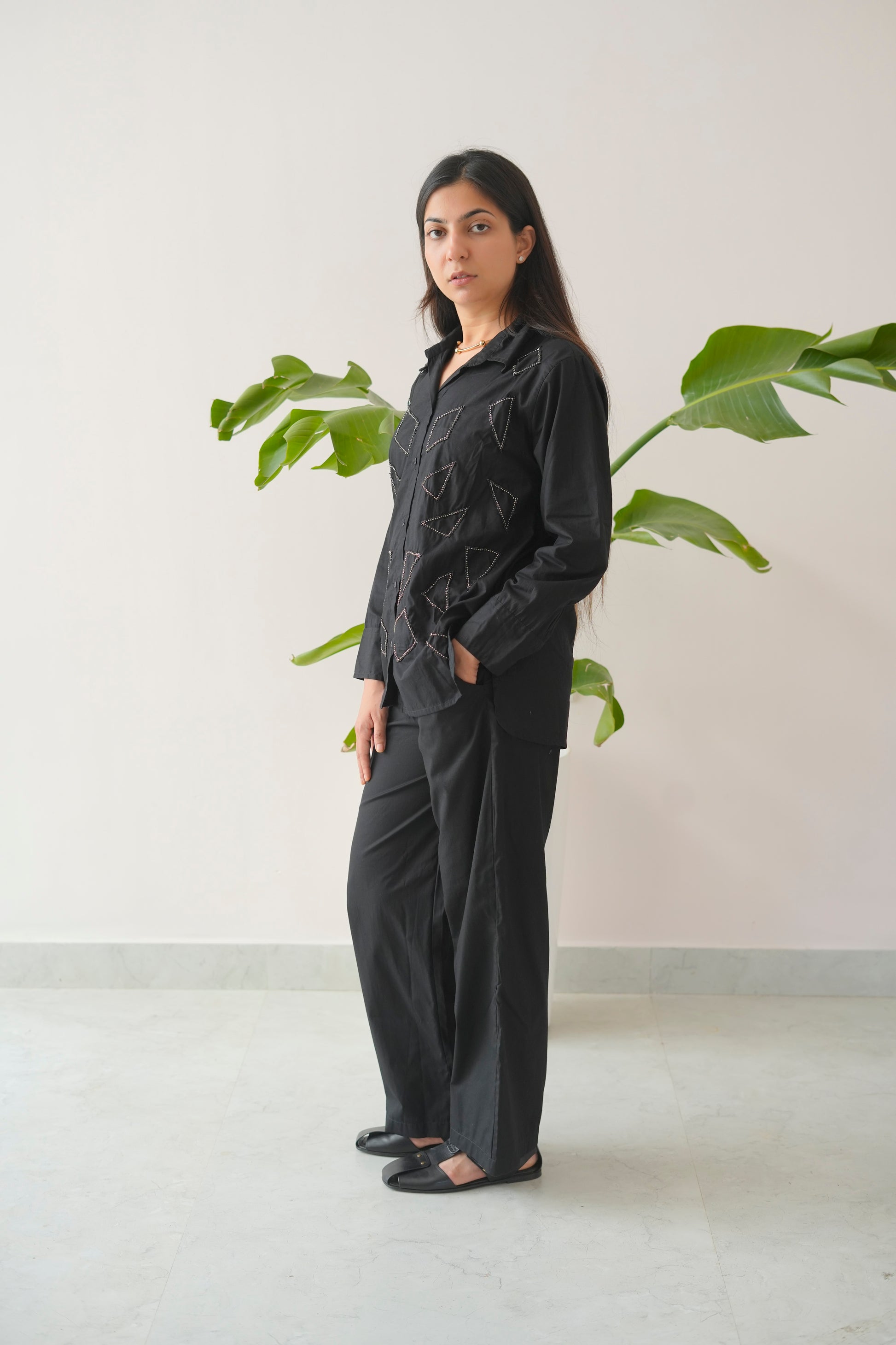 Woman wearing a black outfit standing in front of a plant with a white background