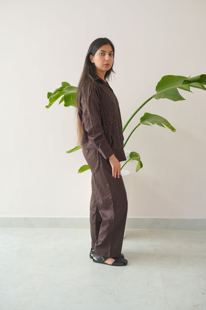 Person wearing a dark outfit standing next to a plant against a white wall.