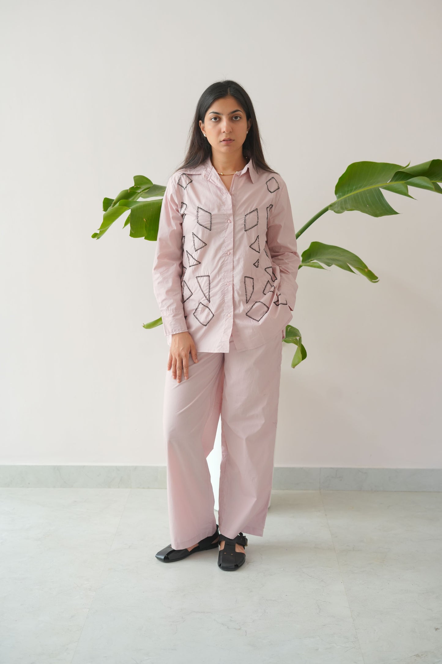 Person wearing a pink outfit with geometric patterns standing against a white wall.