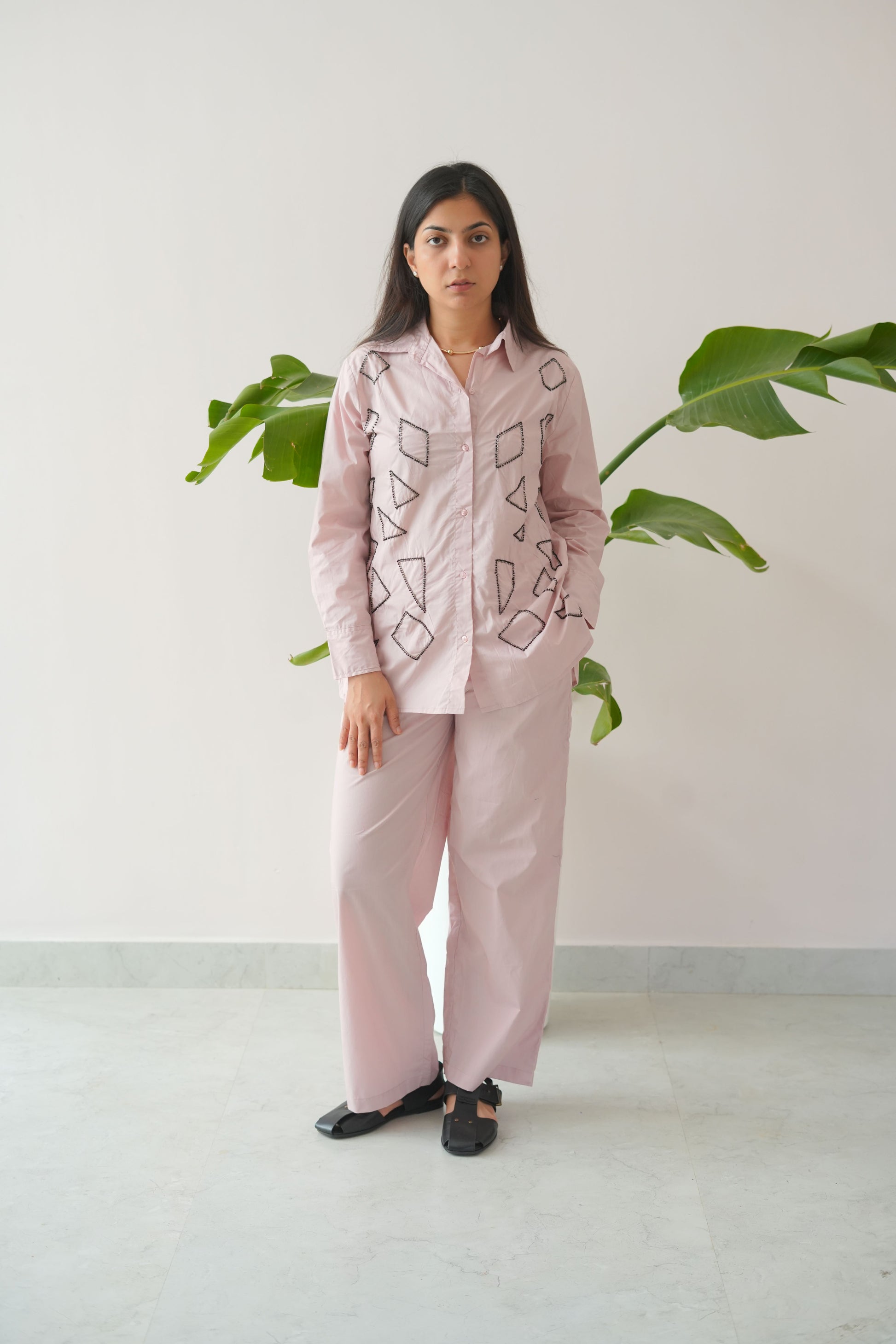 Person wearing a pink outfit with geometric patterns standing against a white wall.