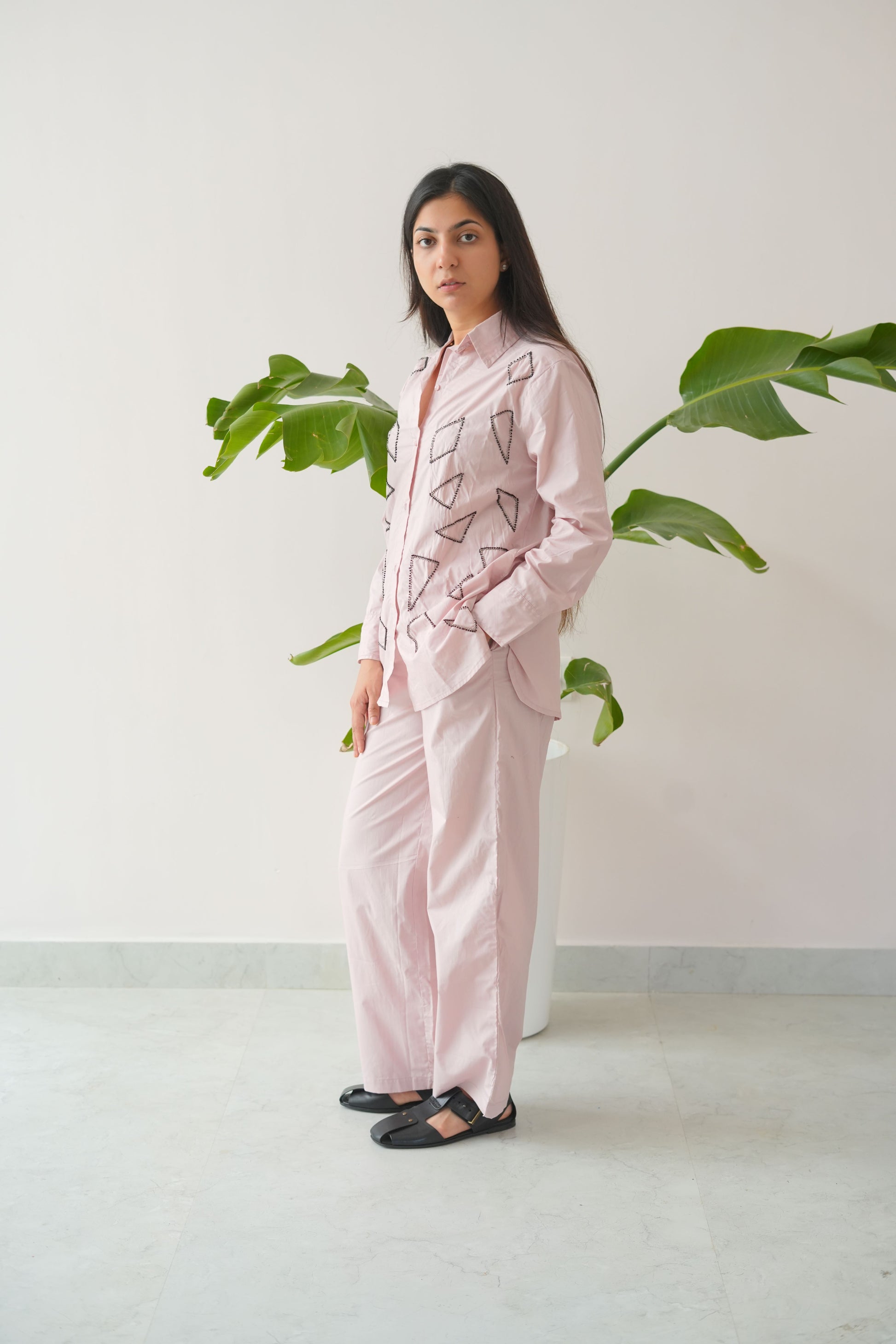Person wearing a pink outfit with geometric patterns standing against a white wall with green plants.