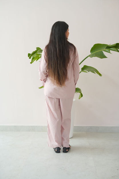 Person wearing a pink outfit standing against a white wall with green plants.