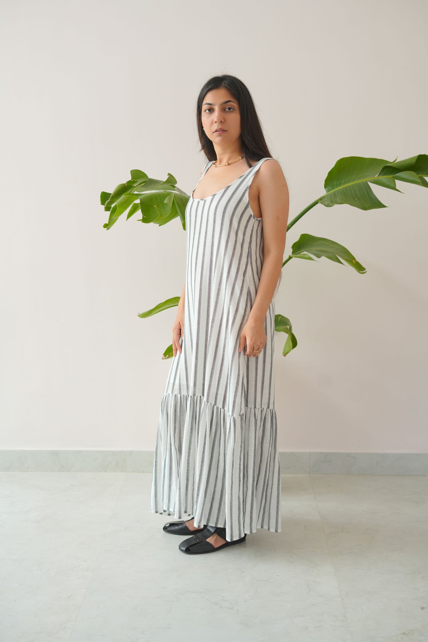 Woman wearing a long, light-colored dress with vertical stripes in a minimal indoor setting.