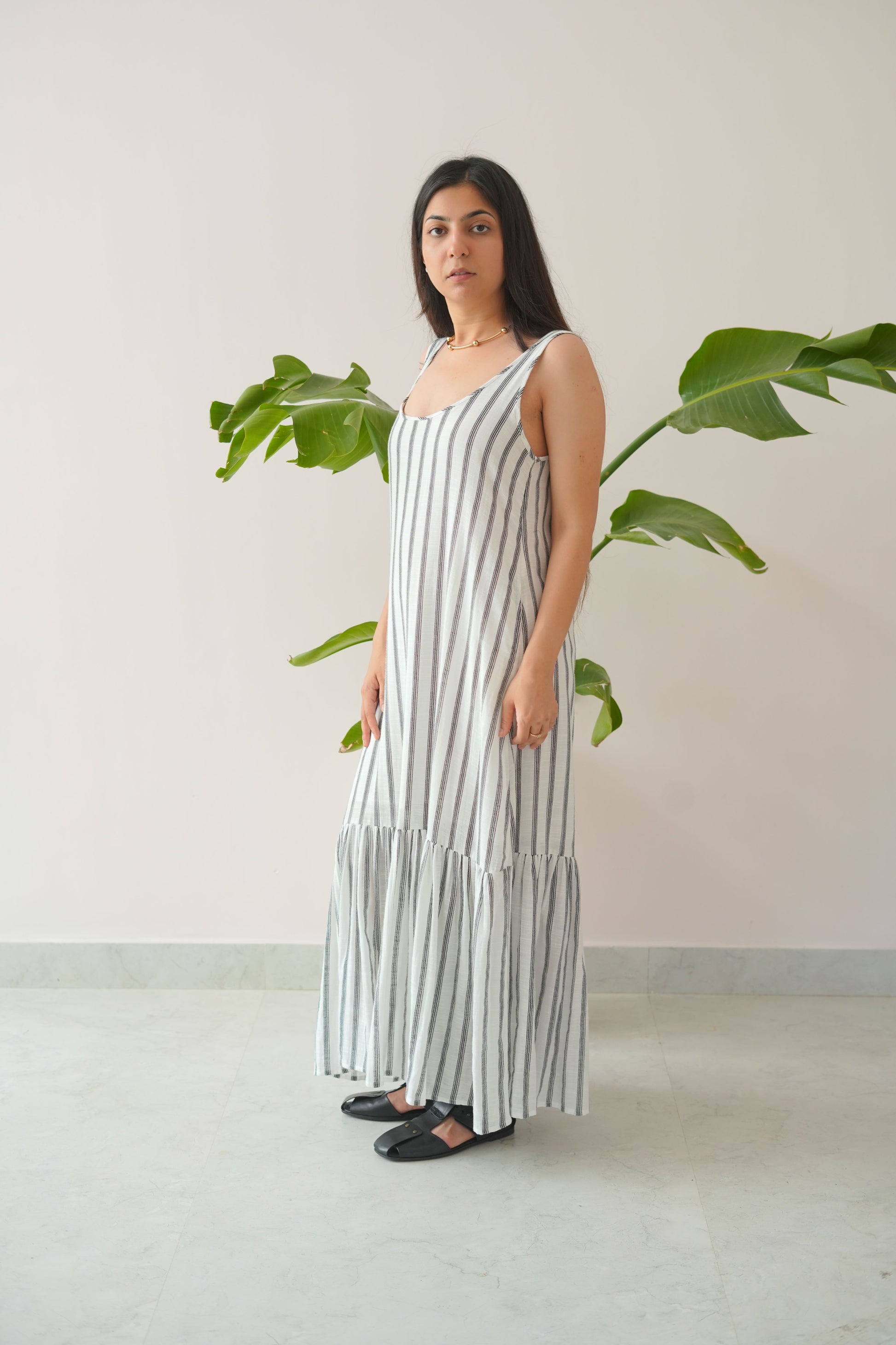 Woman wearing a long, light-colored dress with vertical stripes in a minimal indoor setting.