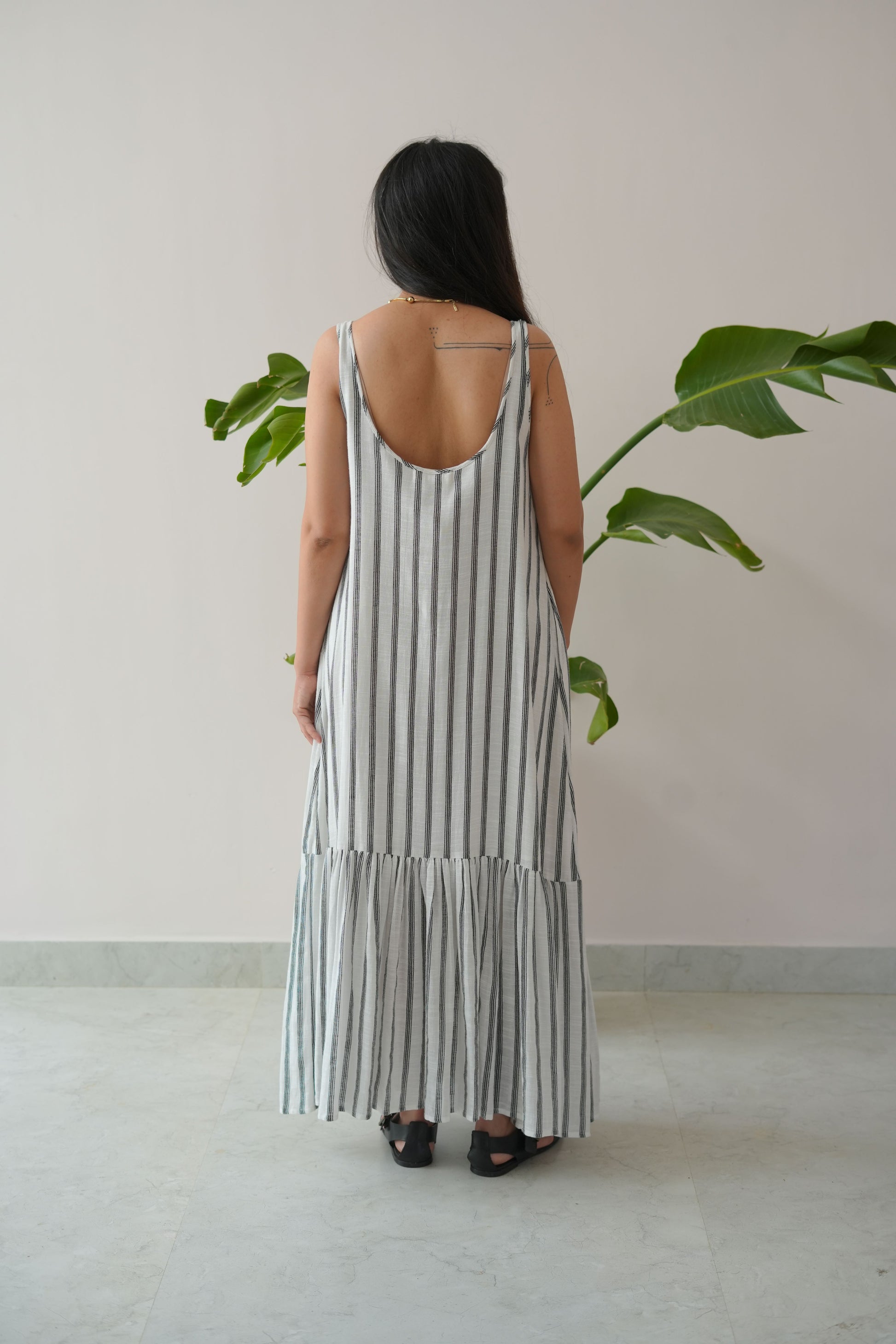 Woman wearing a striped dress standing against a plain wall with a plant in the background