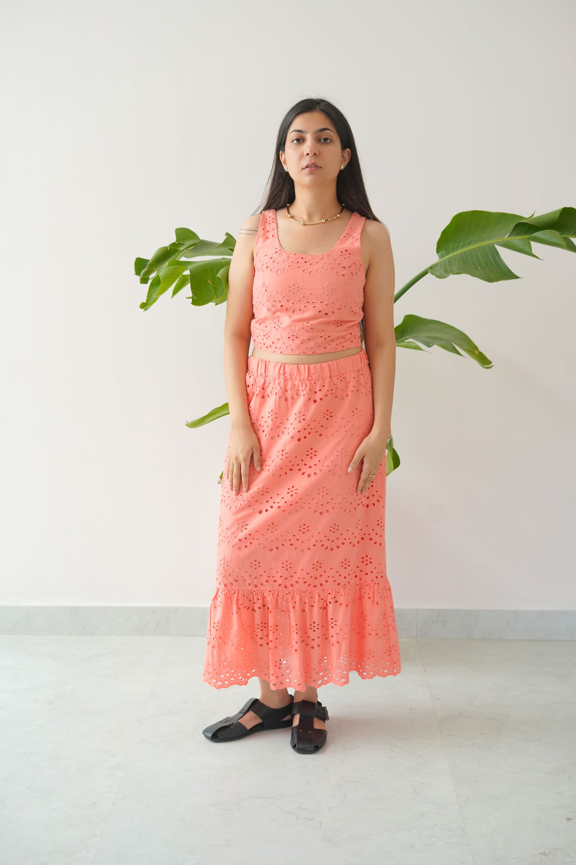 Woman in a pink dress standing between two green plants on a white background