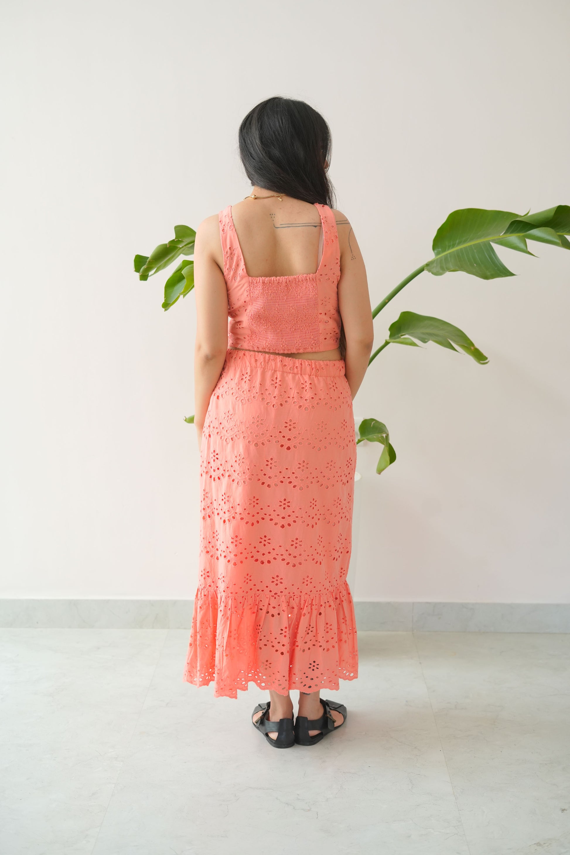 Woman in a pink dress standing against a white wall with green leaves.