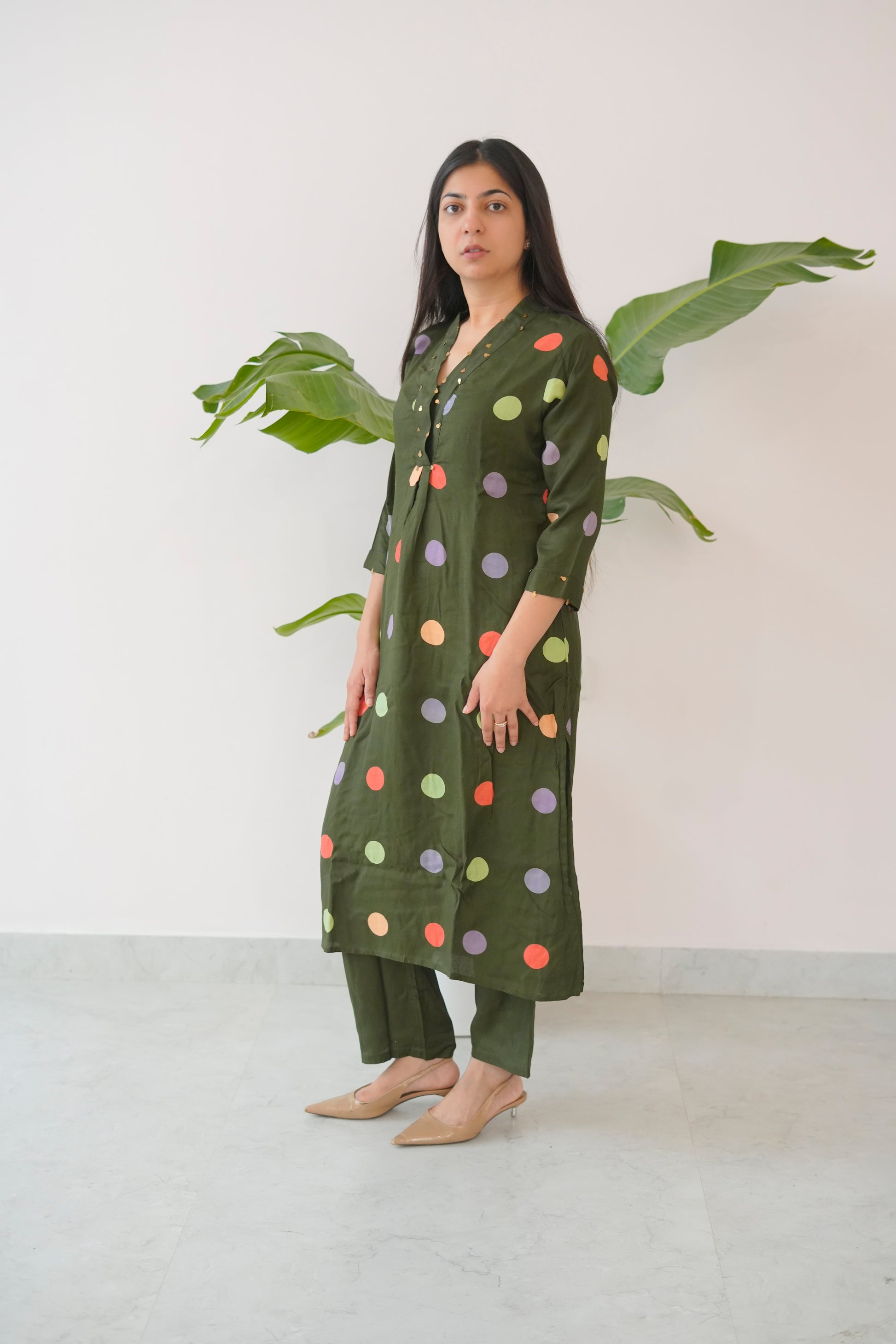 Woman wearing a green polka dot dress with a plant in the background