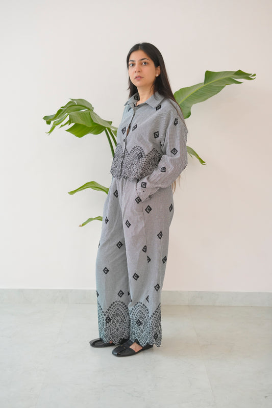 Person wearing a gray patterned outfit standing in front of a plant
