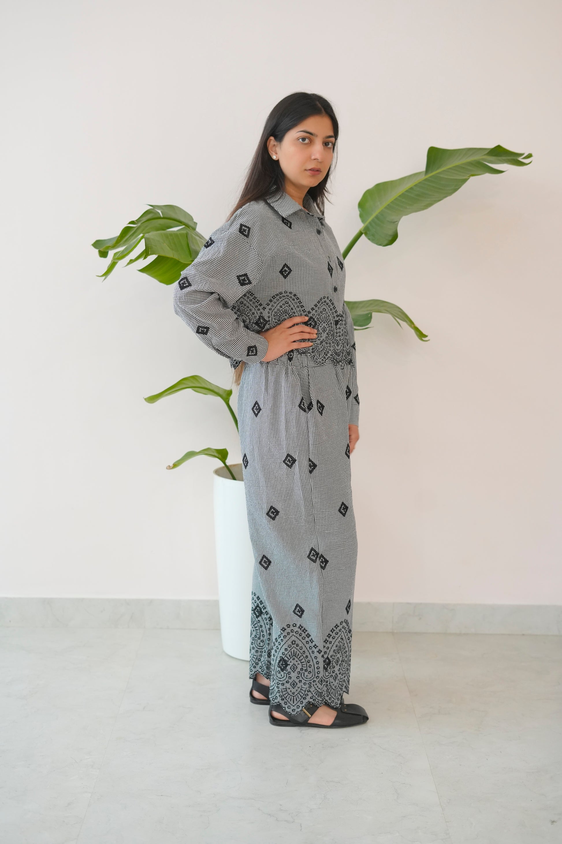 Woman wearing a patterned outfit standing next to a plant indoors.