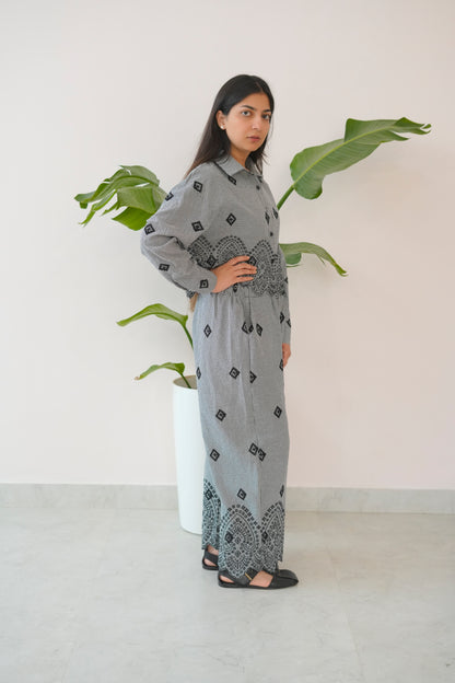 Woman wearing a patterned outfit standing next to a plant indoors.