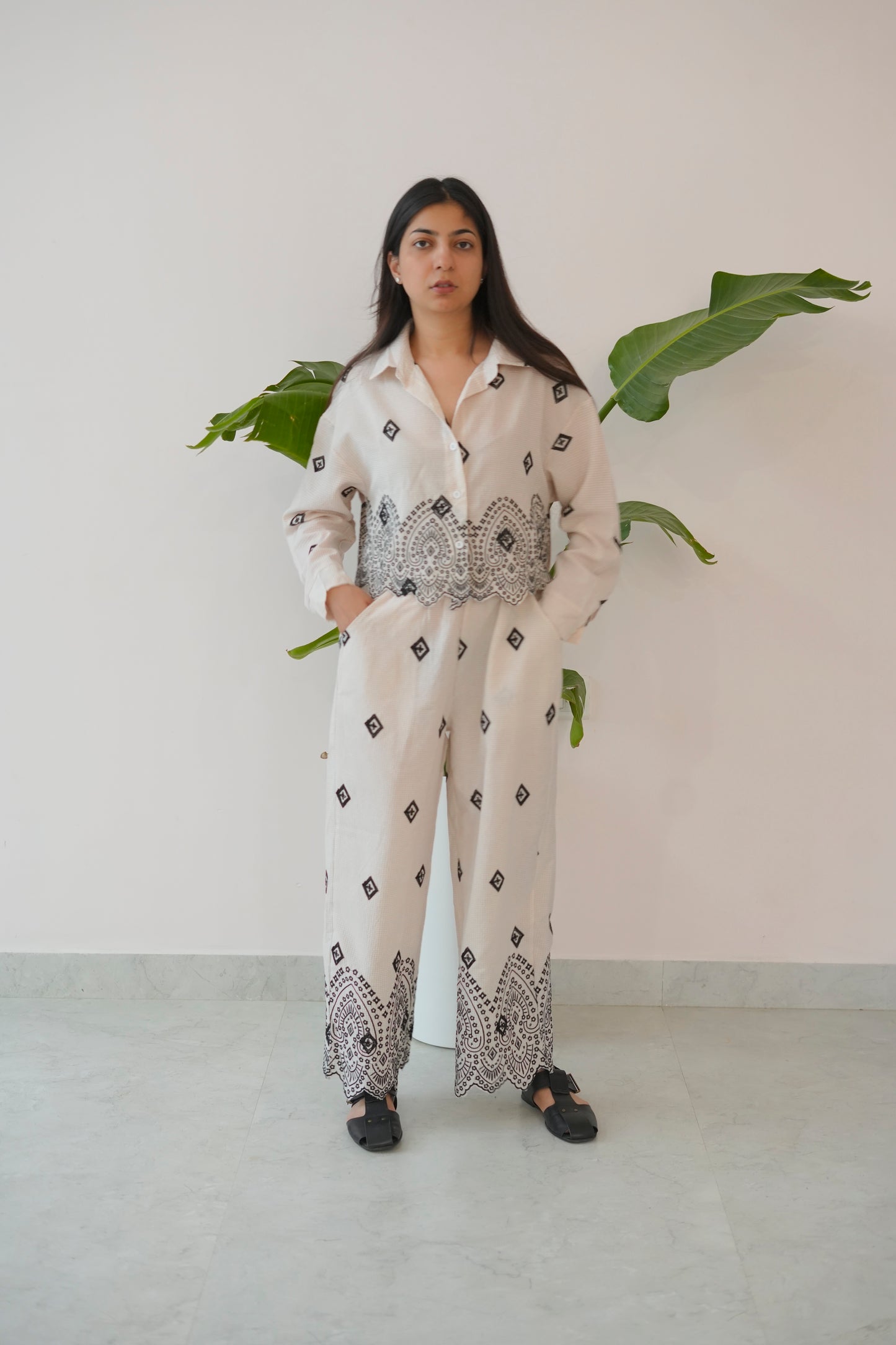 Woman wearing a white outfit with black patterns standing against a plain background