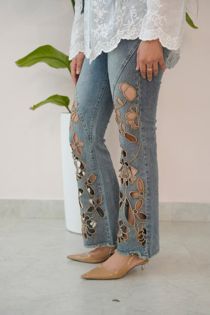 Person wearing floral embroidered jeans with a white lace top against a neutral background