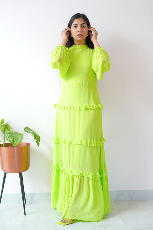 Woman wearing a bright green dress standing indoors with a plant in the background