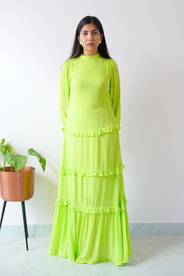 Woman wearing a bright green dress standing against a white wall with a plant in the background.