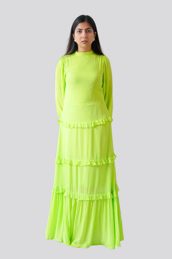 Woman wearing a bright green dress standing against a white wall with a plant in the background.