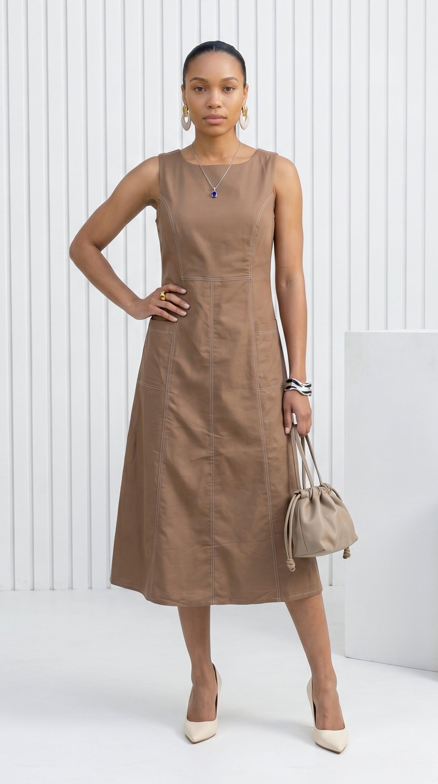 Woman wearing a brown dress holding a beige handbag against a white background