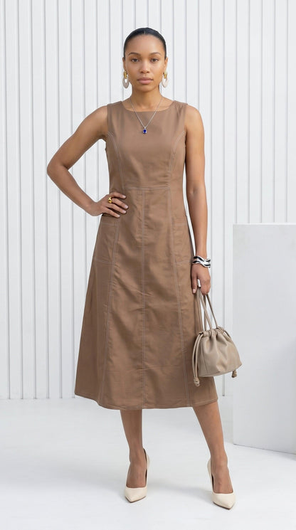 Woman wearing a brown dress holding a beige handbag against a white background